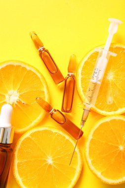 C vitamini, şırınga, sarı zemin üzerinde gerekli yağ ve portakal dilimleri bulunan ampuller.