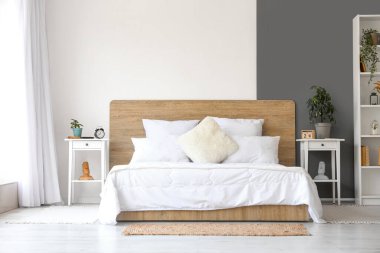 Yatak odasının içinde beyaz yatak odası ve komodinin üzerinde çalar saat var.