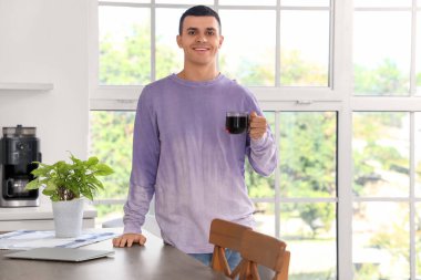 Yakışıklı genç adam mutfakta kahve içiyor.