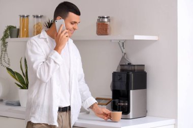 Bir fincan kahveyle yakışıklı genç adam mutfakta telefonla konuşuyor.