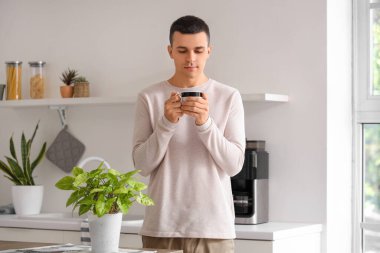 Evdeki mutfakta bir fincan kahveyle yakışıklı bir genç adam.