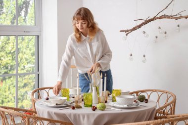 Şükran Günü yemeği için masa dekore eden genç ve güzel bir kadın. Yemek odasında balkabakları ve mumlarla birlikte.