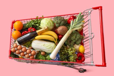 Pembe arka planda yiyecek dolu alışveriş arabası.