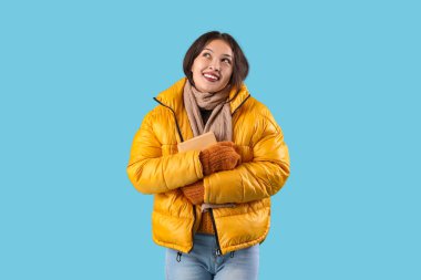 Mavi arka planda kitabı olan sıcak eşarplı güzel Asyalı kadın.