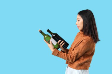 Güzel Asyalı kadın mavi arka planda şarap şişeleriyle