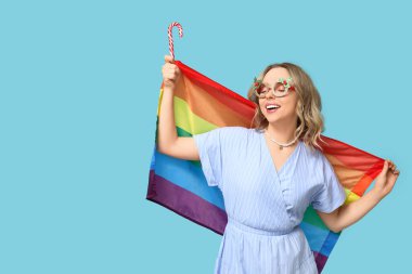 Dekoratif gözlüklü, LGBT bayrağı ve mavi arka planda şeker kamışı olan güzel bir kadın. Noel kutlaması