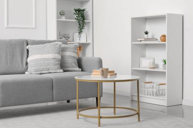 Gri kanepe, masa ve raf üniteleriyle aydınlık oturma odasının içinde.