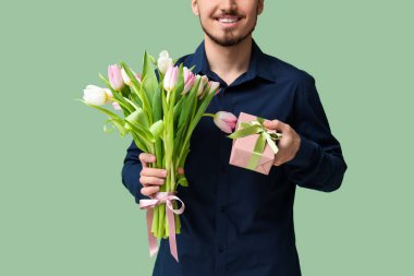 Bir buket güzel lalesi ve yeşil arka planda hediye kutusu olan genç bir adam. Uluslararası Kadınlar Günü