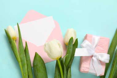 Boş kartlı zarf, hediye kutusu ve turkuaz arka planda beyaz laleler.