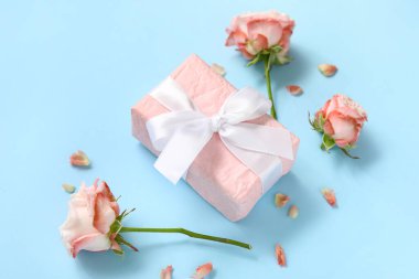 Mavi arka planda güller ve taç yaprakları olan hediye kutusu