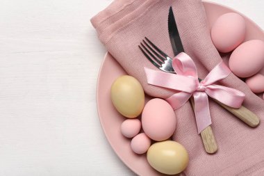 Paskalya yumurtaları, peçete ve beyaz ahşap arka planda çatal bıçak seti olan güzel bir masa.