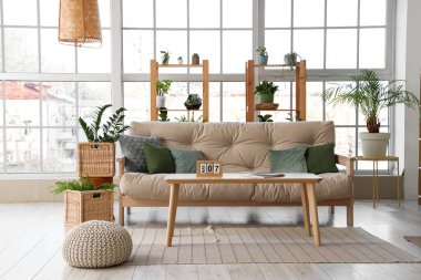 Kanepesi, masası, çiçekleri, rafları ve penceresi olan geniş bir oturma odası.