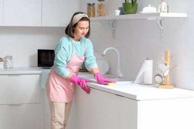 Young woman cleaning kitchen counter with sponge