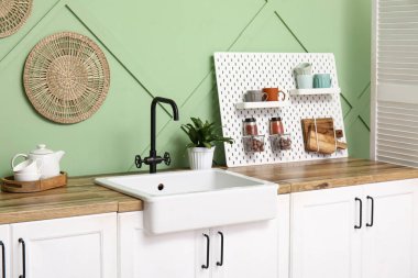 Tahta, lavabo ve beyaz tezgahlar mutfaktaki yeşil duvarın yanında.