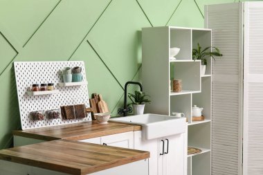 Tahta, beyaz tezgah ve askı modern mutfağın içindeki yeşil duvarın yanında.