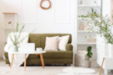 Yeşil kanepeli şık bir oda, kahve masası ve çiçek açan dallar, bulanık bir manzara.