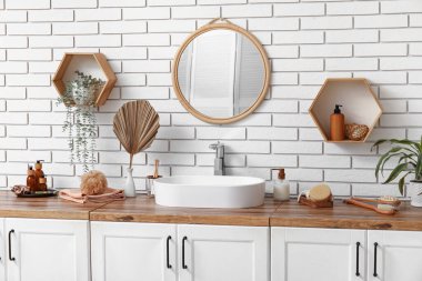 Lavabo, banyo malzemeleri çekmeceler, ayna ve raflar banyodaki beyaz tuğla duvar.