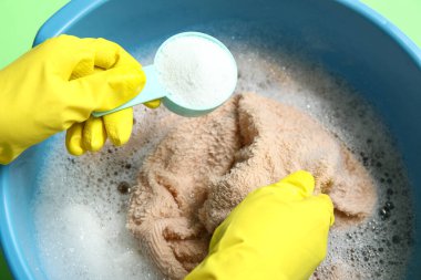 Plastik eldivenli kadın plastik leğende çamaşırlara deterjan ekliyor.