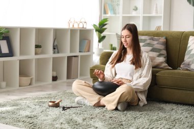 Evde halıda glukofon çalan genç bir kadın.
