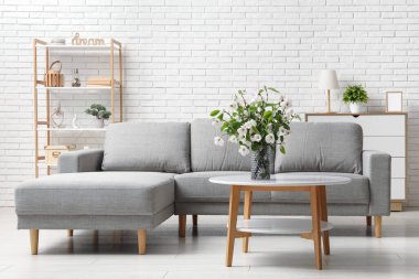 Gri kanepesi, kahve masası ve çiçek açan ağaç dalları olan şık bir oturma odası.