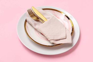 Pembe arka planda altın çatal bıçak takımı olan güzel bir masa.