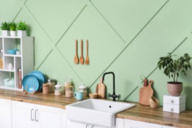 Yeşil duvarın yanında tezgah, lavabo ve çatal bıçak ile modern mutfağın bulanık görüntüsü