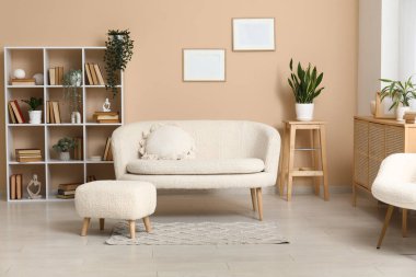 Kitaplık ve ev çiçekleri şık oturma odasındaki beyaz kanepenin yanında.