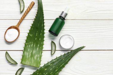 Aloe Vera yaprakları, kavanoz ve beyaz ahşap arka planda bir şişe kozmetik ürünü, yakın plan.