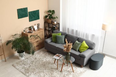 Siyah kanepesi, çiçekleri, çekmeceleri ve sehpası olan şık bir oturma odası.