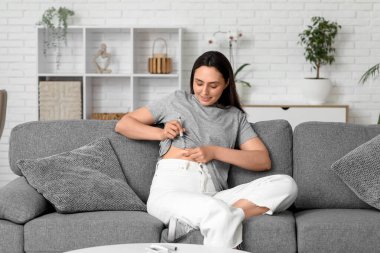 Şeker hastası genç bir kadın evdeki kanepede tükenmez kalem kullanıyor.