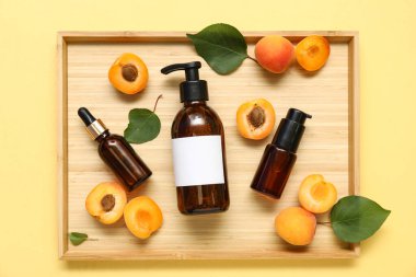 Sarı arka planda taze kayısıları olan farklı kozmetik ürünleri.