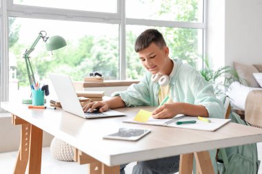 Teenage boy studying with laptop at table in bedroom