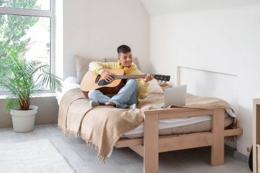 Teenage boy playing guitar in bedroom