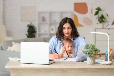 Cute little baby and young mother working with laptop while writing in notebook on maternity leave at home clipart