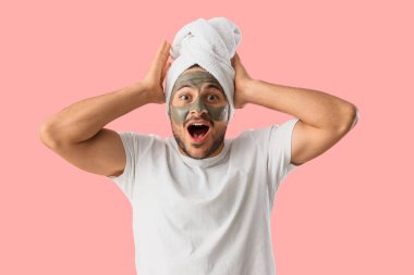 Yüzünde kozmetik kil maskesi olan yakışıklı, genç ve şaşkın bir adam.