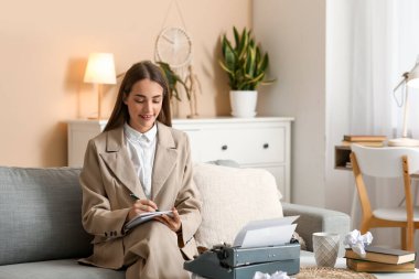 Evdeki kanepede daktiloyla daktilo yazan güzel, mutlu bir kadın yazar.