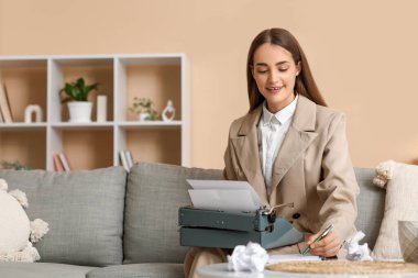 Evdeki kanepede daktiloyla daktilo yazan güzel, mutlu bir kadın yazar.