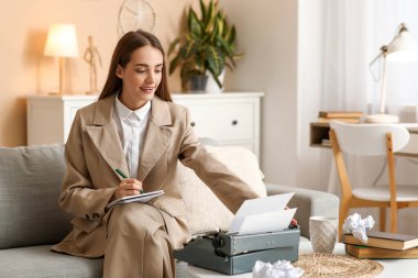 Evdeki kanepede daktiloyla daktilo yazan güzel, mutlu bir kadın yazar.