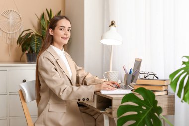 Dizüstü bilgisayarı, dizüstü bilgisayarı ve bir fincan çayı olan güzel bir kadın yazar masada oturuyor.