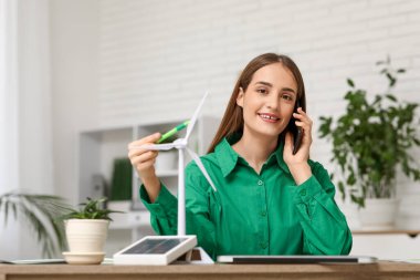 Ofiste rüzgar türbini modeliyle cep telefonuyla konuşan kadın mühendis.