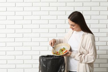 Beyaz tuğladan yapılmış çöp kutusuna organik yiyecekler atan genç bir kadın. Atık geri dönüşüm kavramı