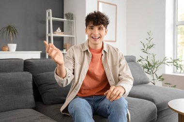 Gülümseyen genç adam evdeki kanepede görüntülü sohbet ediyor.