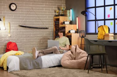 Erkek öğrenci geceleri yatak odasında dizüstü bilgisayar kullanıyor.