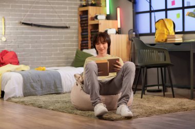 Erkek öğrenci geceleri yatak odasında kitap okuyor.