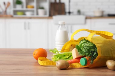 Mutfaktaki ahşap masada farklı taze ürünler bulunan sarı alışveriş çantası.