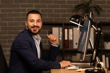 Geceleri ofiste bilgisayarla çalışan gülümseyen işadamı.