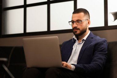 Genç işadamı geceleri koltukta dizüstü bilgisayarla çalışıyor.