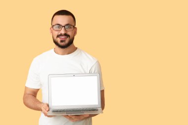 Turuncu arka planda boş dizüstü bilgisayarı olan genç bir adam.