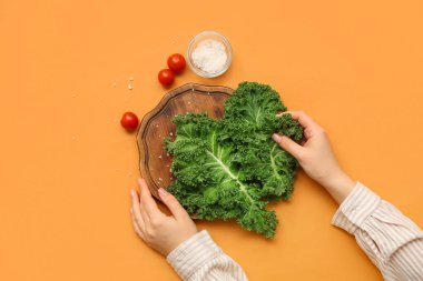 Turuncu arka planda taze lahana yaprakları ve domateslerle dolu tahta tahtası olan kadın eller.