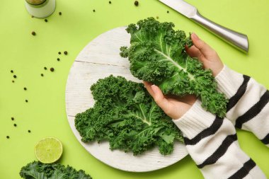 Beyaz ahşap tahta tahtası ve yeşil arka planda yeşil lahana yaprakları ve limonu olan kadın elleri.